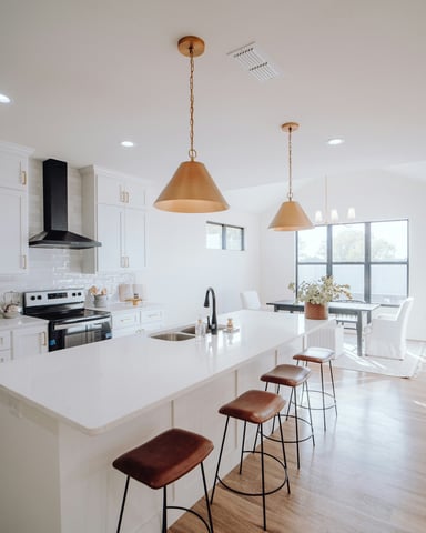 Bright white kitchen with gold pendant lights, white island and leather bar stools