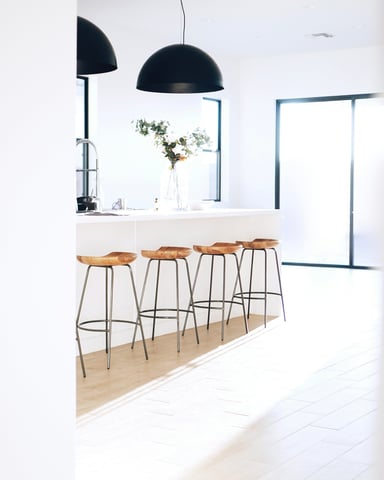 Bright white open-plan kitchen with wood bar stools and black pendant lights