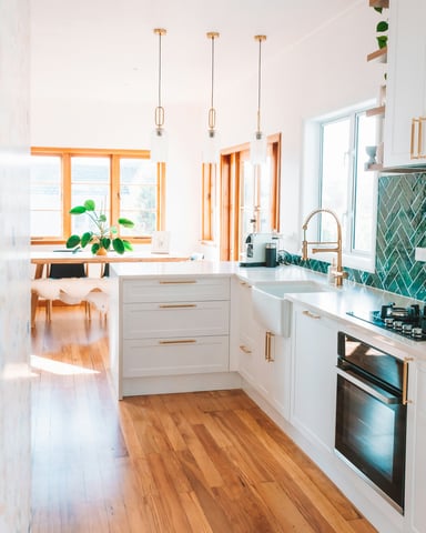 Bright white kitchen with teal tile backsplash, warm wood floors and brass fixtures