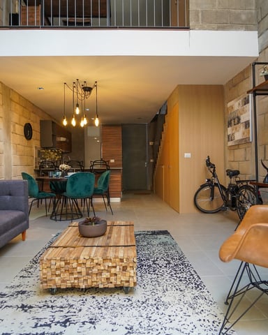 Modern loft living room with gray sofa, tan leather chair, wooden coffee table, wall-mounted TV, and bicycle storage