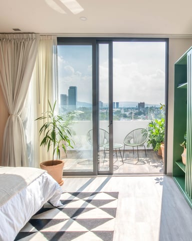 Modern bedroom with city skyline view through floor-to-ceiling glass doors opening to balcony with seating