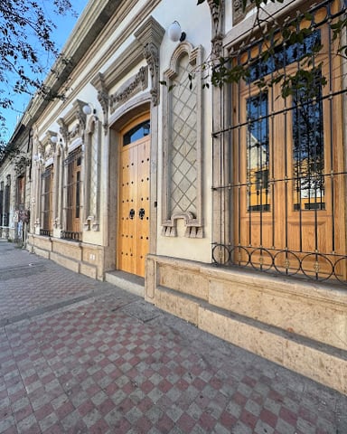 Historic building facade with ornate white columns, wooden doors, and barred windows along a paved street