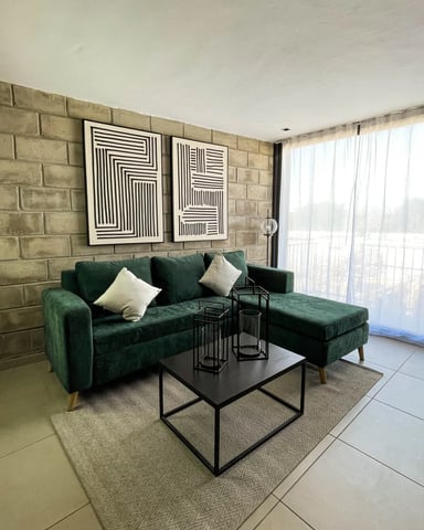 Sala con sofá de terciopelo verde, pared de ladrillo expuesto y cortinas translúcidas