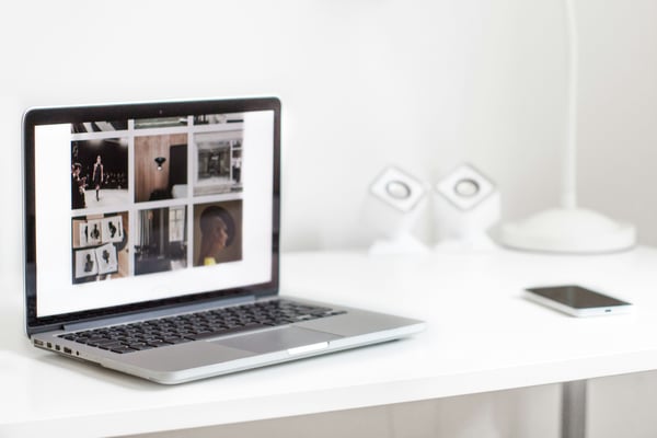 Laptop on white desk displaying a photo grid, representing property listing and marketing