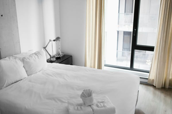 Bright white bedroom with fresh folded towels and floor-to-ceiling windows