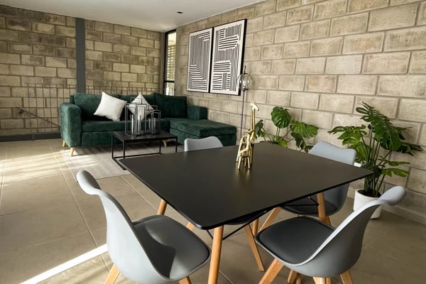 Modern open-plan living space with black dining table, green sofa, brick walls, and pendant lighting