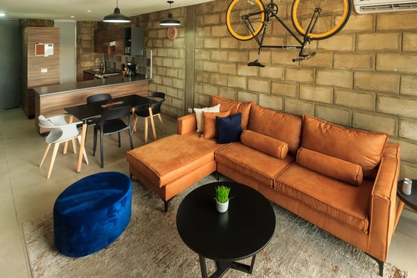 Modern loft living room with orange leather sofa, blue velvet ottoman, black round table, and two yellow bikes mounted on brick wall
