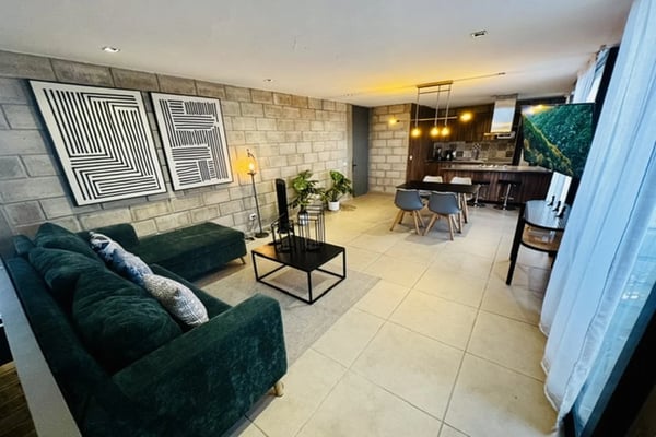 Modern open-plan living room with dark green sofa, black coffee table, geometric wall art, and kitchen bar area with stools