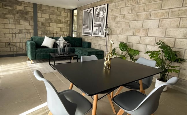 Modern open-plan living space with black dining table, green sofa, brick walls, and pendant lighting