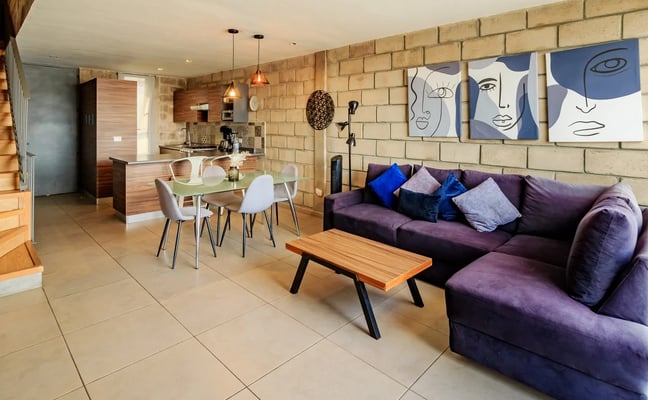 Open-plan living area with purple sectional sofa, dining table, brick wall, and modern abstract artwork