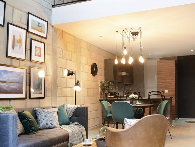 Modern loft living room with gray sofa, tan leather chair, mezzanine balcony, and open kitchen visible in background